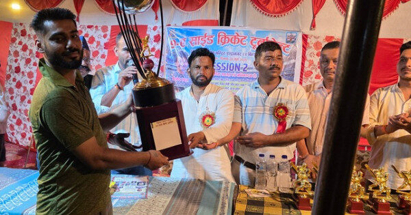 बिन्दुखत्ता नाइट क्रिकेट टूर्नामेंट की पुरस्कार वितरण समारोह की तस्वीर, जिसमें किच्छा टीम के कप्तान ललित फाइनल जीतने के बाद बड़ी ट्रॉफी ग्रहण कर रहे हैं। ट्रॉफी उन्हें जिला पंचायत सदस्य कमलेश चंदोला द्वारा दी जा रही है। मंच पर अन्य अतिथि व आयोजन समिति के सदस्य भी मौजूद हैं